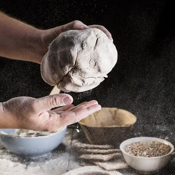 Mani infarinate lavorano un panetto di impasto nel buio del laboratorio